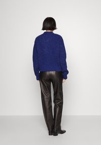 Blå stickad tröja med en texturerad yta, kombinerad med högmidjade svarta läderbyxor. Silhuetten är avslappnad.