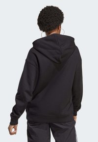 Svart fleece-hoodie med en rymlig huva, ribbade muddarna och en avslappnad passform. Materialet är mjukt med en slät textur.