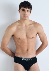 Zwarte herenboxers met een zachte elastische tailleband met "DIESEL" branding, een gladde textuur en een snug fit, gemodelleerd op een shirtloze persoon.