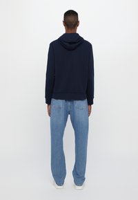 Felpa blu marina con cappuccio regolabile, abbinata a jeans azzurri a vestibilità comoda. L'outfit presenta una vestibilità rilassata e una texture morbida.