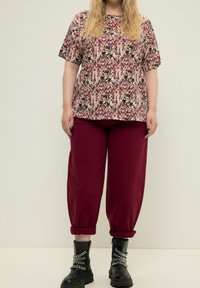 Lyhyet hiharat kukkakuosisessa paidassa burgundin sävyissä, yhdistettyinä löysiin burgundinvärisiin housuihin ja mustiin sotakengissä, joissa on ketjusomisteita.