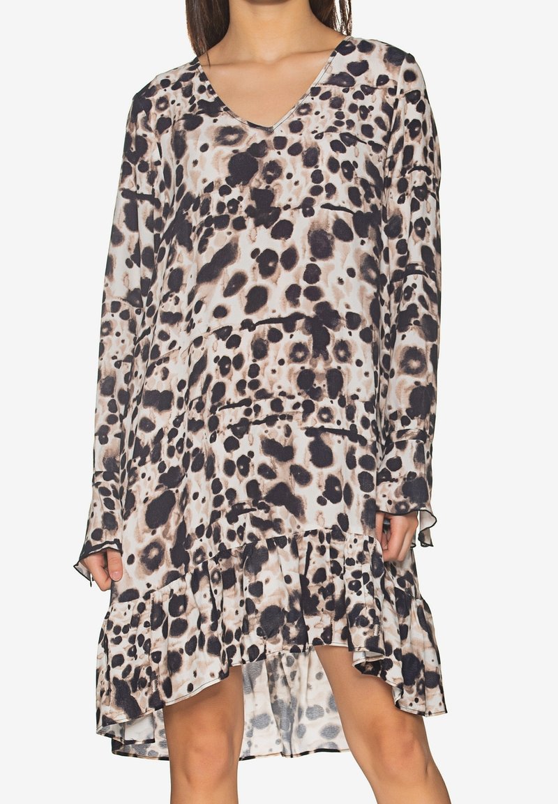 Kvinna som bär en långärmad klänning med V-hals, i beige och svart djurtryck med rynkad asymmetrisk fåll.