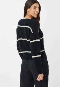 Marine gestreepte trui met roomkleurige horizontale lijnen, losse pasvorm, gebreide textuur, ronde hals en ribbelrand, gedragen over een zwarte broek.