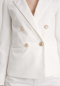 Bílý dvouřadý blejzr s texturovanou tkaninou, se zlatými knoflíky a bočními kapsami. Čistý, dobře střižený silueta.