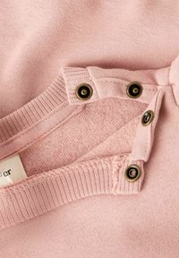 Tessuto del maglione rosa con una consistenza morbida, caratterizzato da quattro bottoni a pressione in ottone e un collo a costine. L'imbottitura interna ha una finitura pelosa.
