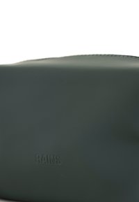 Borsa impermeabile verde con una texture liscia, forma arrotondata e logo "RAINS" in rilievo sulla parte anteriore. Design minimalista e finitura elegante.