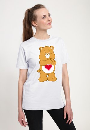 T-shirt blanc présentant un ours brun en cartoon avec un cœur sur son ventre. Le design est imprimé sur un tissu doux en coton.