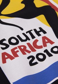 Katoenen stof met een kleurrijk ontwerp met abstracte vormen in zwart, geel, rood en blauw. Tekst luidt "ZUID-AFRIKA 2010."