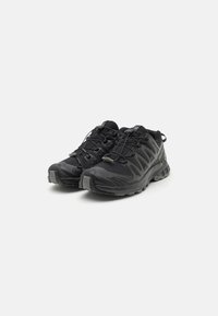 Chaussures de sport noires avec une tige en mesh, des superpositions texturées et une semelle en caoutchouc robuste avec un système de laçage sécurisé.