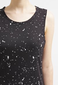 Svart ärmlös topp med rund halsringning, som har ett vitt sprutmönster över tyget för en strukturerad look.