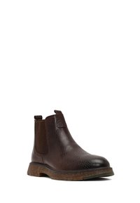 Bota Chelsea de cuero marrón con superficie texturizada, paneles laterales elásticos y suela gruesa marrón. Diseño simple sin patrones visibles.