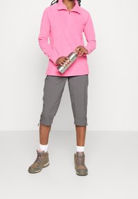 Sudadera de forro polar rosa con media cremallera, pantalones recortados grises con cremalleras en el dobladillo, y botas de senderismo marrones con cordones.