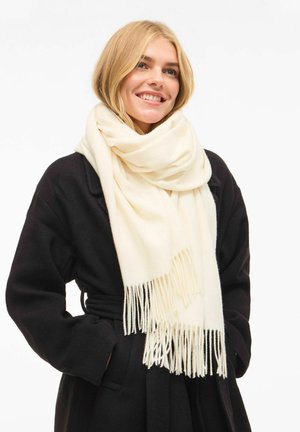 Hvit skjerf laget av mykt stoff med frynsete kanter, båret over en svart frakk. Skjerfet er løst viklet rundt halsen.