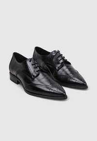 Zapatos de cuero negro con punta afilada, perforaciones decorativas y diseño de cordones. Acabado suave y tacón bajo.