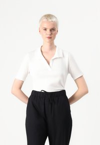 Chemise polo blanche à manches courtes avec col, assortie à un pantalon noir à taille élastique avec cordon de serrage. Texture lisse, design simple.