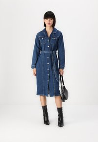 Jeans φόρεμα με κουμπιά και ζώνη στη μέση, μακριά μανίκια, τσέπες στο στήθος και μήκος στο γόνατο. Συνδυασμένο με μαύρες μποτάκια ankle και μαύρη τσάντα.