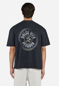 Tricou din bumbac negru cu un grafic mare pe spate, având textul "DOLCE VITA PEGADOR" și un motif vegetal, croială oversized și mâneci scurte.