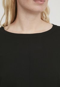 Juoda dryžuota megzta palaidinė su plačia apvali iškirpte ir subtiliais vertikaliais siūlės akcentais, pabrėžianti lygią tekstūrą ir priglundantį dizainą.
