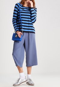 Sininen ja mustaraidallinen neulepaita, väljät siniset culottes-housut, hopeiset kengät ja pieni sininen käsilaukku. Sileä pinta, rento muotoilu ja löysä istuvuus.