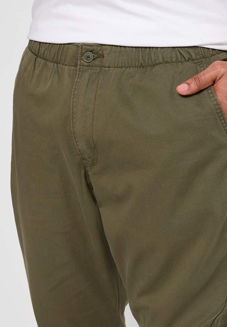 Pantaloni verde oliva realizzati in tessuto leggero con cintura elastica e chiusura a bottone, dotati di tasche laterali e una superficie liscia.