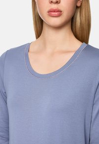 Himmelblaues Langarmshirt mit einem Rundhalsausschnitt, versehen mit dezenten rosa Nähten entlang des Ausschnitts. Sanfte, weiche Stoffoberfläche.