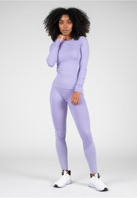 Paarse long-sleeve sporttop en leggings, met een gladde textuur en geribbelde accenten, gecombineerd met witte sportschoenen.