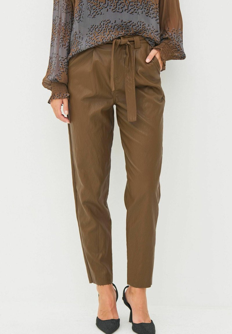 Rjave, visoko pasovane hlače v slogu papirnatega vrečka z zavezanjem, z gladko teksturo in zoženimi nogami. V kombinaciji z vzorčasto bluzo.