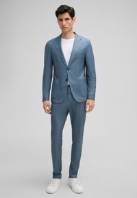 Lichtblauw op maat gemaakt kostuum met een textuurafwerking, voorzien van een blazer met twee knopen, dubbele voorkantzakken en slim-fit broeken, gecombineerd met witte sneakers.