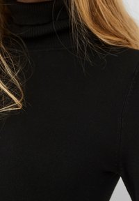 Czarny sweter golf w żebrowanym wzorze, dopasowany krój z długimi rękawami i wysokim kołnierzem, ukazujący gładką powierzchnię.