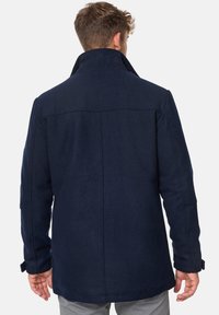 Manteau en mélange de laine bleu marine avec un col haut, des coutures visibles, des poches latérales et des poignets ajustables, conçu pour la chaleur et le confort.