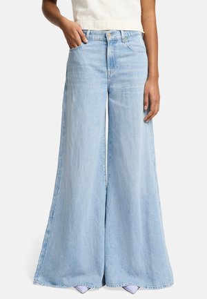 Kvinde iført lyseblå denimjeans med vide ben og høj talje, kombineret med en hvid cropped top og lavendelfarvede spidse sko.