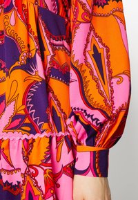 Kleurijke jurk met abstract paisleypatroon in roze, paars en oranje. Lange mouwen met elastische manchetten en gerimpelde details bij de taille.
