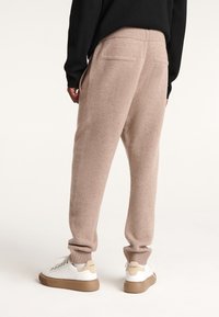 Fleece-Sweatpants in hellbeige mit gerippten Bündchen, zwei Gesäßtaschen, kombiniert mit weißen Sneakers, die einen sandfarbenen Akzent und eine dicke Sohle haben.