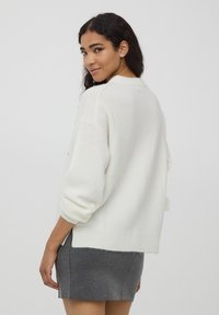 Biała swetrowa bluzka o luźnym kroju, z opadającymi rękawami i prążkowanym dołem. Połączona z szaro-mini spódnicą, prezentującą miękką teksturę.