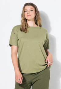 Oliwkowo-zielona koszulka z krótkim rękawem ozdobiona złotymi gwiazdkami, zestawiona z teksturowanymi ciemnozielonymi spodniami. Gładka bawełniana tkanina.