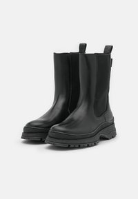 Černé kožené kotníkové boty s elastickými bočními panely, kulatou špičkou, silnou černou gumovou podrážkou a poutky pro snadné obouvání.