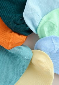 Sept chaussettes pliées en cercle avec les couleurs bleu sarcelle, orange, jaune pâle, bleu clair, vert menthe et vert foncé sur un fond blanc.