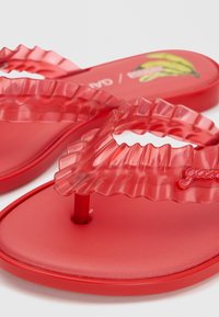 Κόκκινα ημιδιαφανή σανδάλια thong με βολάν και λαστιχένια σόλα, με μικρή λεπτομέρεια λογότυπου και γραφικό μπανάνας στην εσωτερική σόλα.