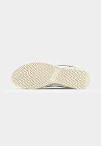 Shoe sole with a light cream color, featuring a zigzag pattern and a branded logo in the center. Material appears rubber or synthetic.