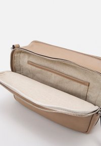 Skórzana torba w kolorze brązowym z zamkiem błyskawicznym. Wnętrze wykończone beżową tkaniną, posiada kieszeń na drobiazgi oraz dodatkową wyściółkę.