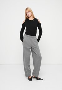 Top negro de manga larga con hombros descubiertos, combinado con pantalones grises de pierna ancha. La modelo lleva tacones negros puntiagudos. Diseño sencillo y moderno.