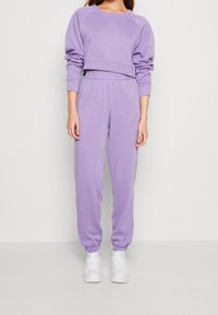 Sudadera de algodón morada con mangas raglán, combinada con joggers morados a juego. Ambos cuentan con bandas elásticas en los puños y la cintura. Zapatillas blancas.