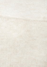 Šviesiai smėlio spalvos megzta medžiaga, pasižyminti smulkia ribiška tekstūra su subtiliais atspalvių pokyčiais ir tolygia audimo rašto struktūra visame paviršiuje.