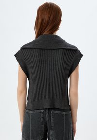 Sømløs striktop i mørkegrå med vertikal ribbete tekstur og en foldet krave bagpå, parret med højhalsede sorte denimshorts.