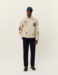 Μπεζ καμβάς μπουφάν με διάφορες εκτυπωμένες εικονογραφήσεις; με φερμουάρ μπροστά, μακριά μανίκια, συνδυασμένο με ναυτικές παντελόνες και ναυτικό καπέλο.