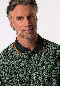 Zelená vzorovaná polo košile s oranžovým límečkem, na hrudi je umístěno logo a má zapínání na knoflíky. Texturovaná, prodyšná tkanina.