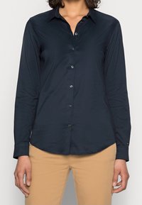 Dark blue button-up shirt with long sleeves, a collared neck, smooth texture, and button closures. Worn over light tan pants.
