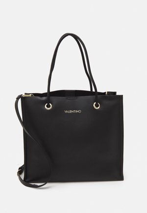 Czarna torba Valentino typu tote z podwójnymi uchwytami, złotymi oczkami i odpinanym paskiem na ramię na jednolitym białym tle.