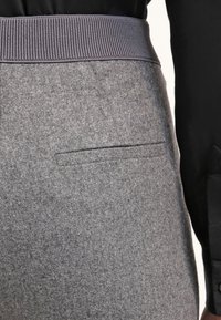 Pantaloni grigi in lana con superficie texturizzata, dotati di una vita a coste scura e una tasca a fessura sul lato.