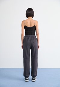 Černý texturovaný crop top s tenkými řetízkami na ramínkách, který je paired s šedými tepláky s elastickými manžetami a detailem zadní kapsy.